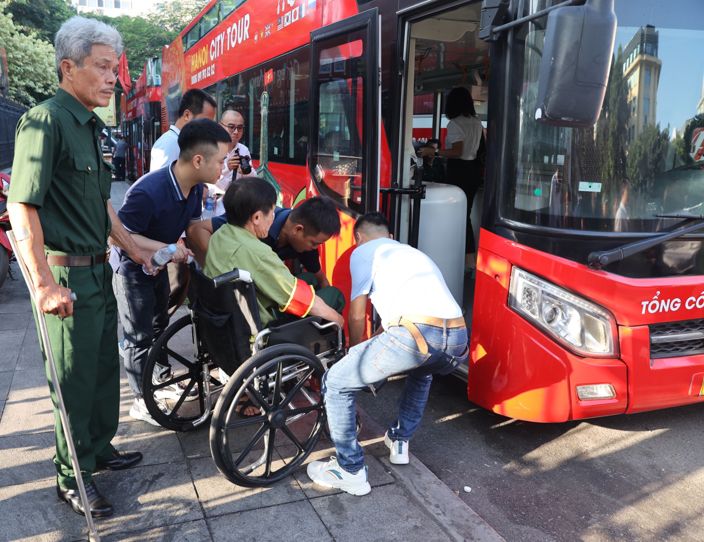 Các đoàn viên hỗ trợ một thương binh nặng di chuyển lên xe buýt hai tầng. (Ảnh: Trọng Tài)