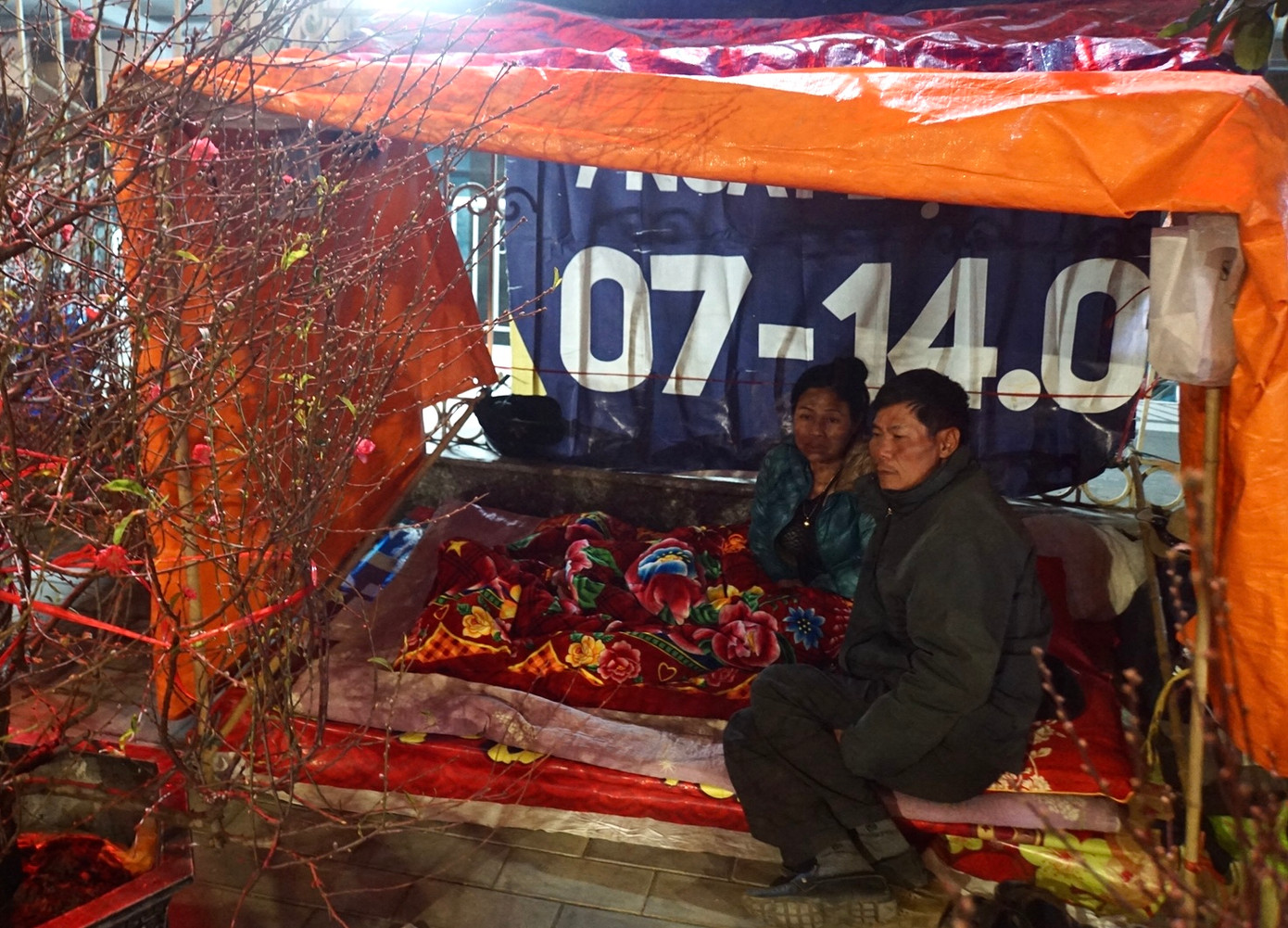 Anh Lương và vợ là chị Nguyễn Thị Phượng trong chiếc lều dựng tạm từ các thanh gỗ, tre và phủ bạt, áo mưa làm mái.