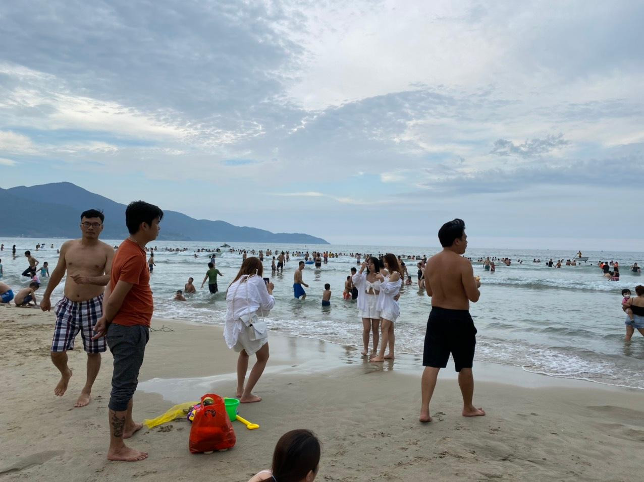 Một nhóm bạn trẻ tạo dáng, check in trên bãi biển đông nghịt người.