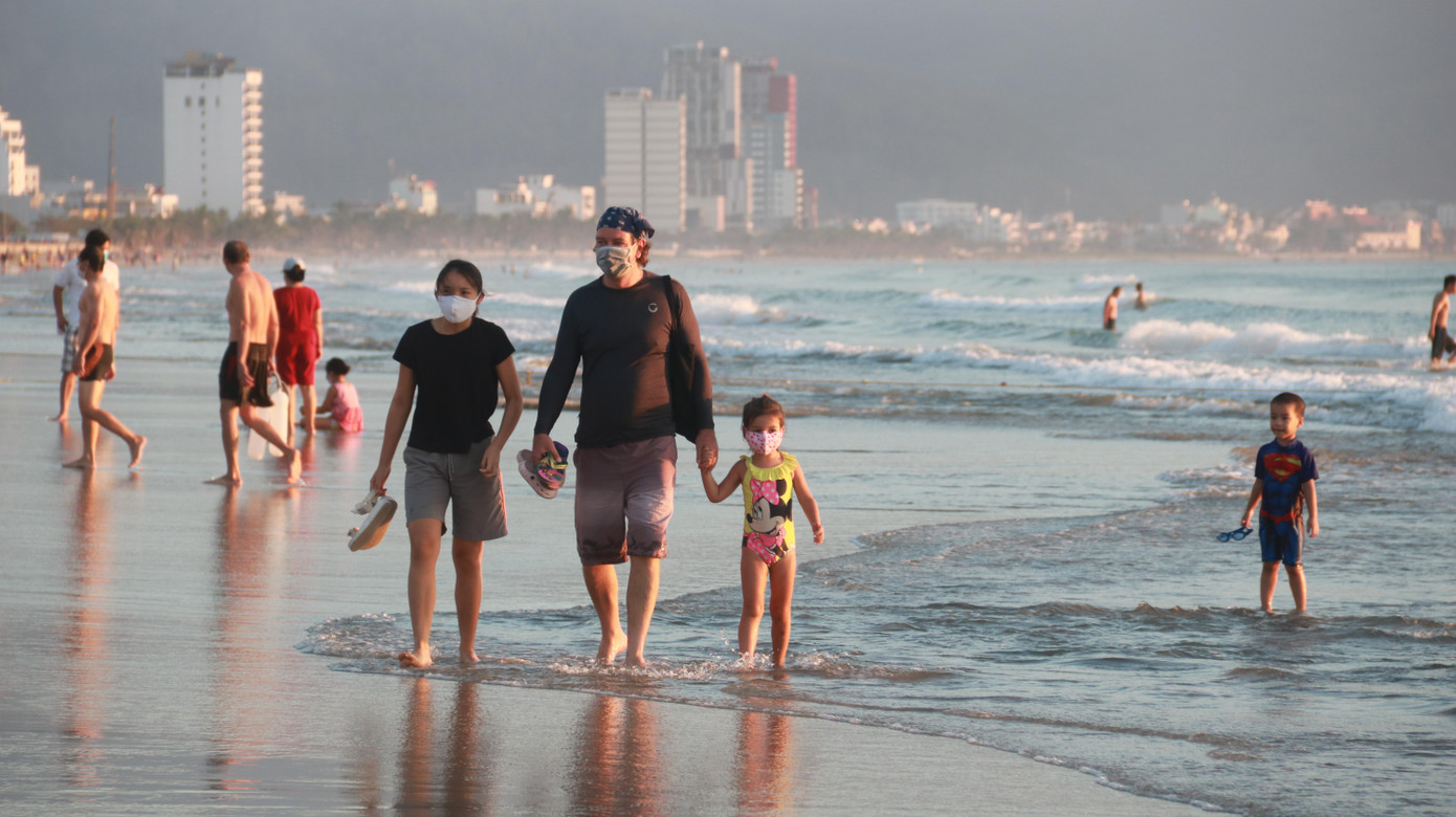 Một gia đình người nước ngoài dắt nhau dạo trên bãi biển.