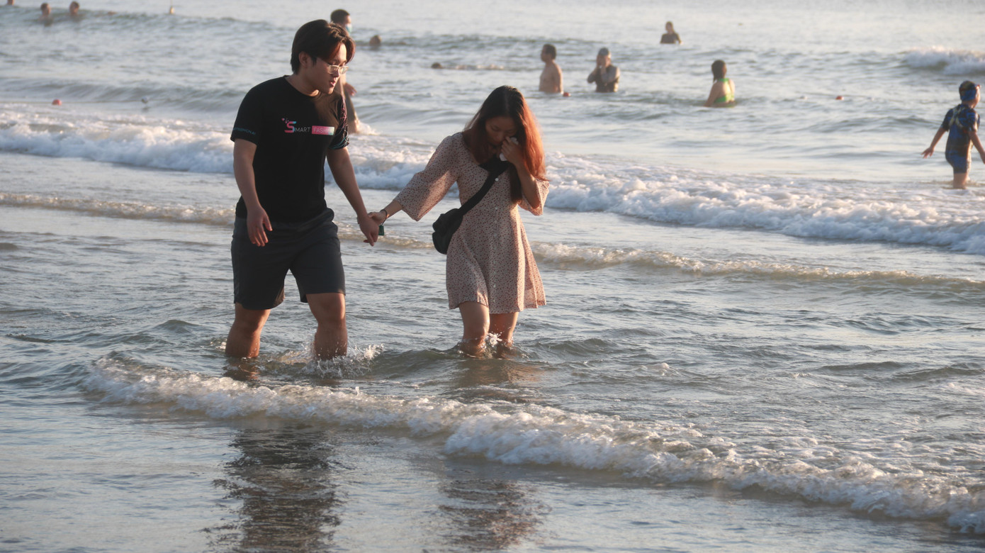 Đôi bạn trẻ tay trong tay đi dạo biển.