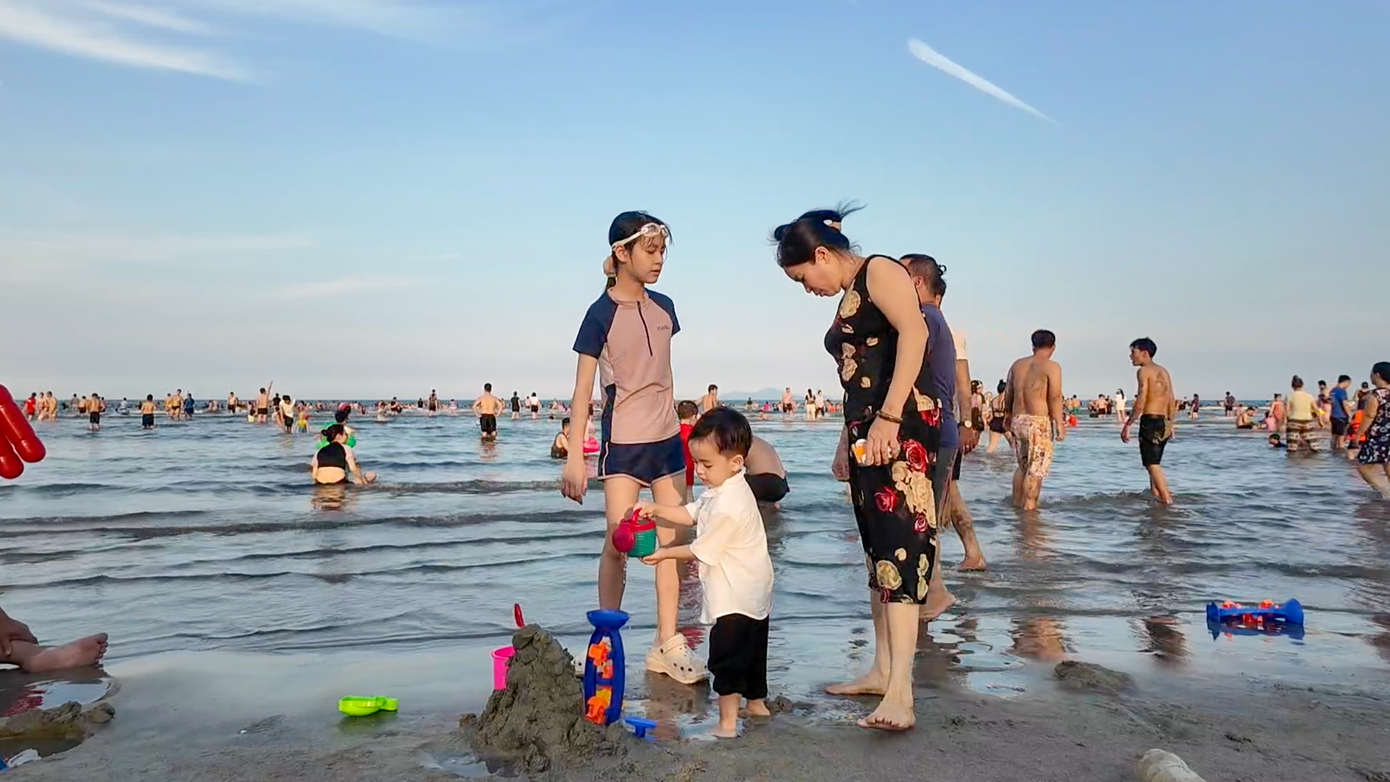 Một gia đình đưa con ra biển chơi đùa trong nắng chiều, mát mẻ.