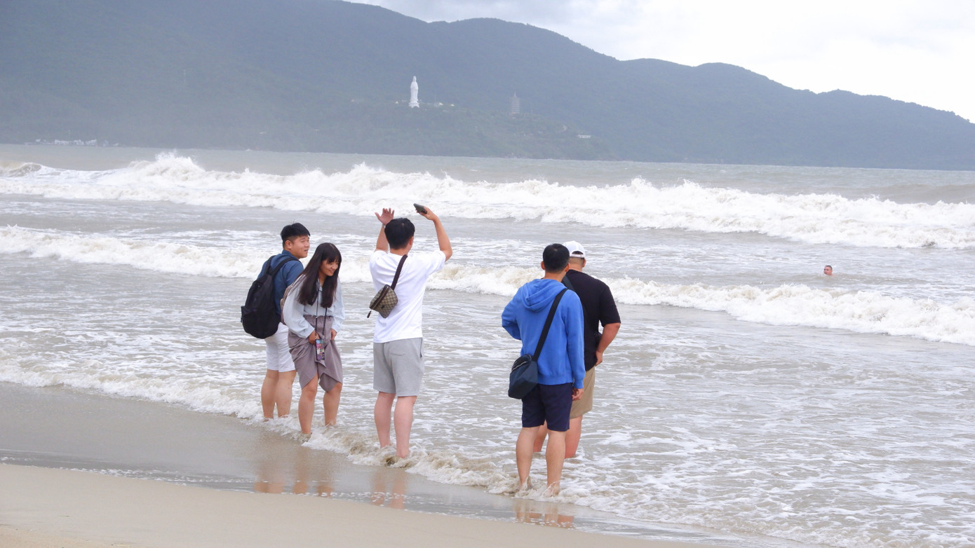 Một nhóm du khách vẫy tay gọi người thân đang bơi ngoài biển, quay vào bờ theo yêu cầu của lực lượng chức năng.