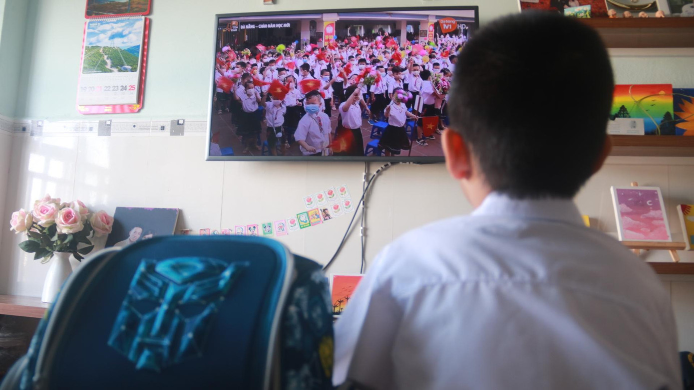 Đúng 7h, chương trình &quot;Chào mừng năm học mới&quot; được đài Phát thanh - Truyền hình Đà Nẵng (DRT) phát sóng. Bé chăm chú theo dõi hình ảnh lễ khai giảng của những năm trước được chiếu trên tivi.