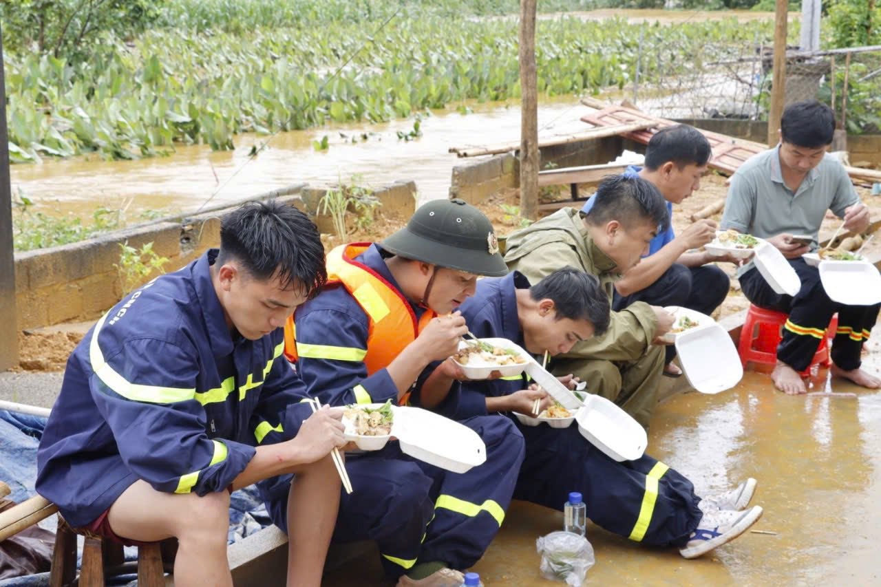 Sau những giờ phút căng mình trong mưa lũ, giúp dân di dời tài sản, cứu nạn cứu hộ, các chiến sĩ công an nhân dân ngồi ăn vội bữa cơm bên vệ đường.