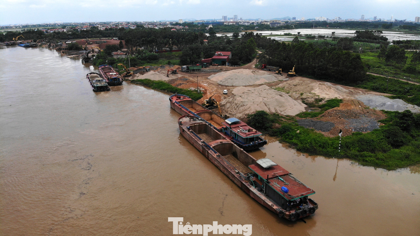 Trên bãi, những núi cát sỏi khổng lồ vẫn nằm “chình ình”. Trên các bãi vật liệu, máy xúc, ủi hoạt động hết công suất, dưới nước tấp nập tàu bè đưa hàng lên bến.