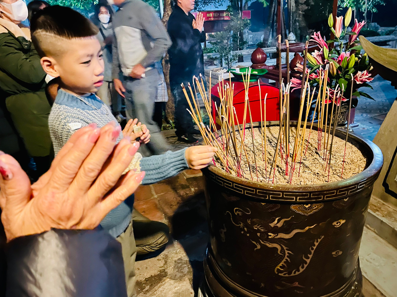 Một em nhỏ được bố mẹ hướng dẫn tự cắm nhang, khấn bái.