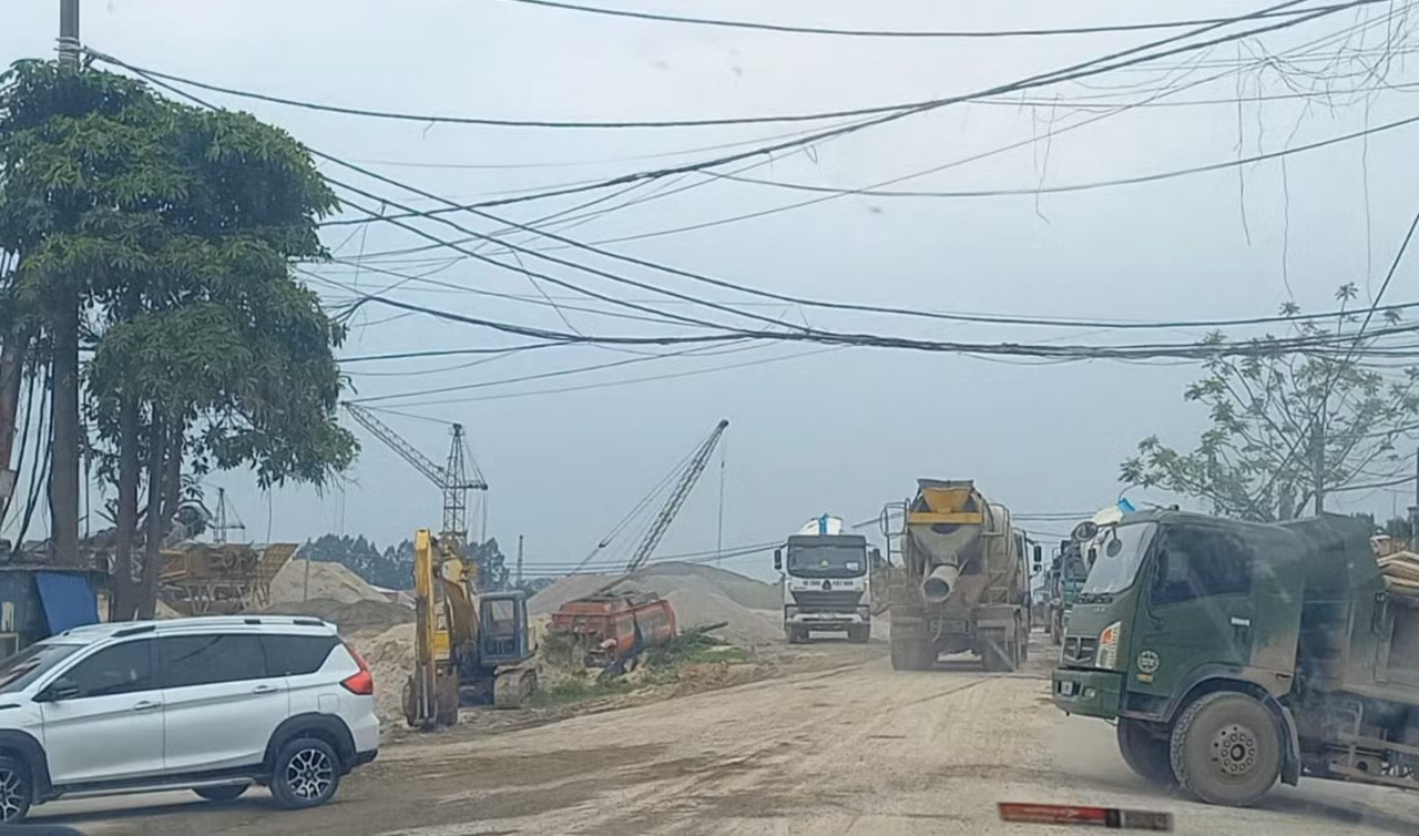 Trên đường đê, xe tải, xe chở bê tông nối đuôi nhau rầm rập chạy. Khói bụi theo các cơn gió mù mịt khắp một khúc đê.