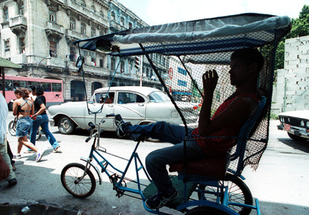 Một lái xe xích lô – phương tiện được coi là taxi ở Cu Ba, đỗ cạnh một xe hơi Mỹ cổ điển tại Havana vào ngày 11/6