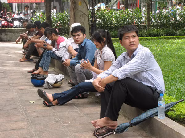 Không muốn chen lấn mua vé, nhiều sĩ tử tìm bóng cây ngồi nghỉ. Ảnh: Trường Phong