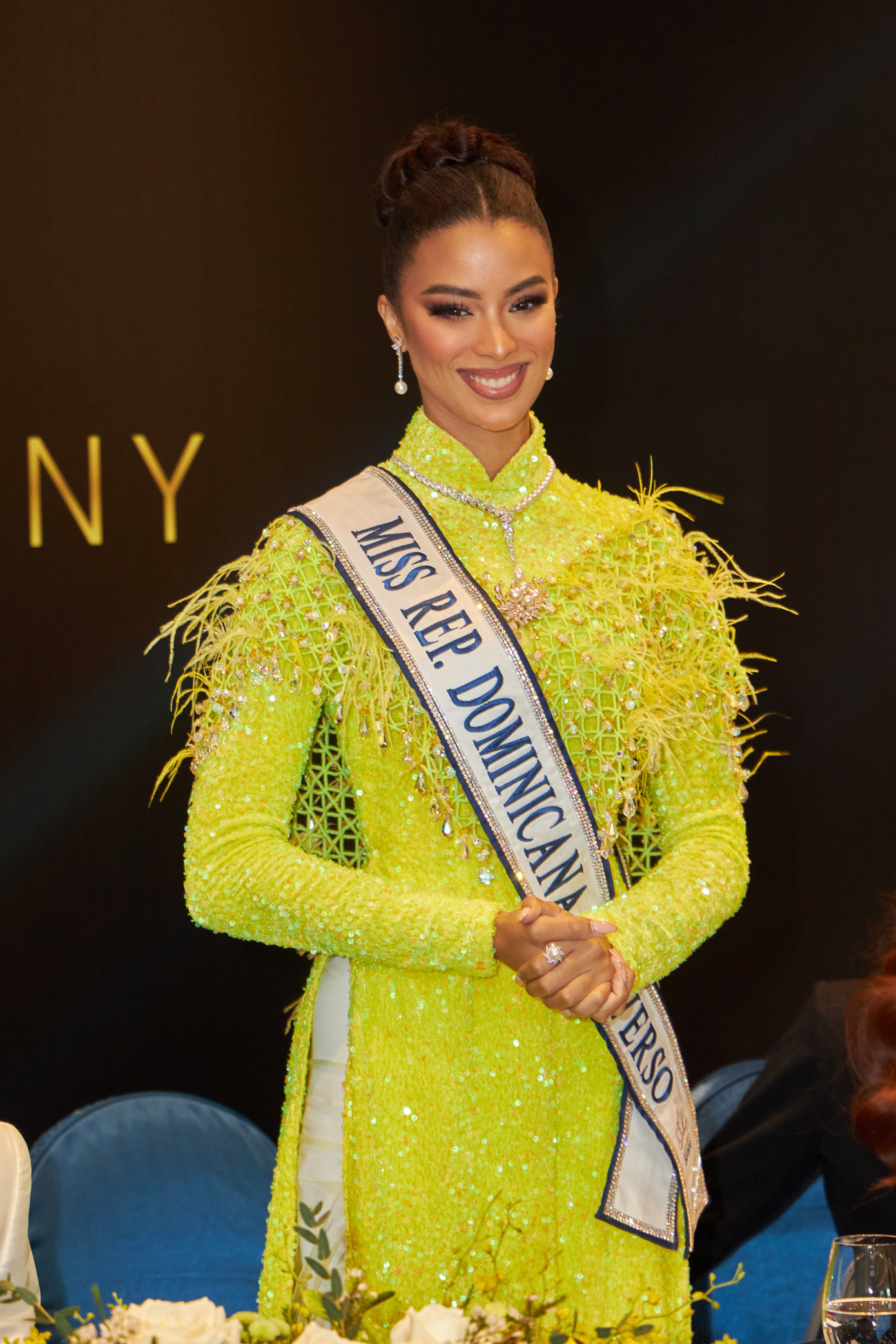 Á hậu 2 Andreína Martínez chọn áo dài tông màu vàng nổi bật với điểm nhấn là những chiếc lông vũ được đính kết tỉ mỉ trên thân áo. Người đẹp chọn cách búi tóc sang trọng, quý phái. Phong cách trang điểm được các chuyên gia make-up người Việt thực hiện cho người đẹp Cộng hòa Dominica giúp cô tỏa sáng hơn tại sự kiện.