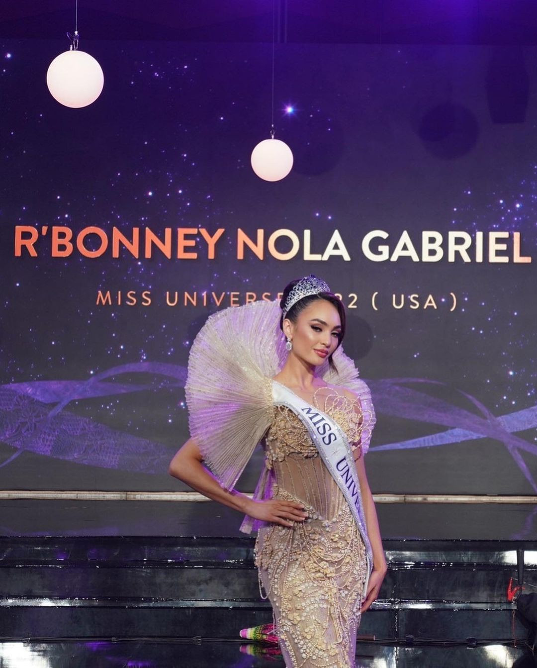 Thiết kế với tông màu vàng gold, đính kết tỉ mỉ. Điểm nhấn là phần cầu vai được tạo phom 3D với chủ đích mang lại vẻ đẹp quyền lực cho người mặc. Tuy nhiên thiết kế này được cho là rườm rà, không tôn vóc dáng của R'Bonney Gabriel. Cô vốn có vóc người nhỏ nhắn, chiều cao khiêm tốn nên thiết kế cồng kềnh khiến người đẹp như bị "dìm dáng".