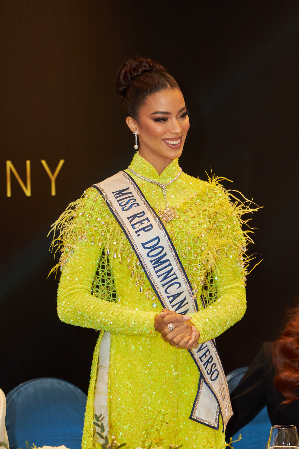 Á hậu 2 Andreína Martínez chọn áo dài tông màu vàng nổi bật với điểm nhấn là những chiếc lông vũ được đính kết tỉ mỉ trên thân áo. Người đẹp chọn cách búi tóc sang trọng, quý phái. Phong cách trang điểm được các chuyên gia make-up người Việt thực hiện cho người đẹp Cộng hòa Dominica giúp cô tỏa sáng hơn tại sự kiện.