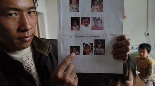 Người đàn ông trưng hình của những đứa trẻ đã bị bắt cóc đem bán. Ảnh: Caing.com