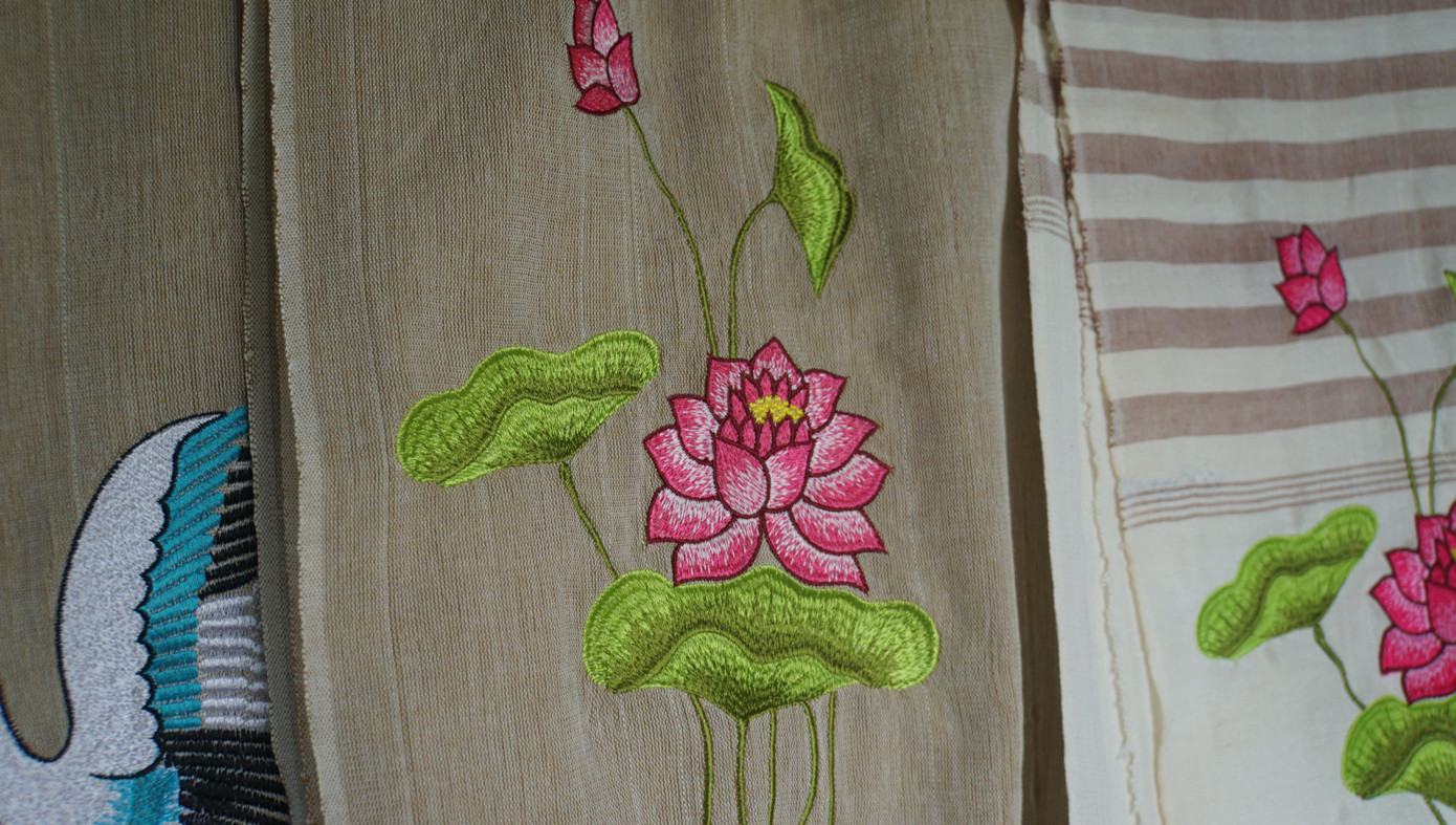 Từ ba màu carô truyền thống, hiện làng nghề làm ra gần trăm mẫu mã khác nhau kết hợp thêu logo, biểu tượng sếu, hoa hồng... Trong ảnh: Khăn thêu hoa sen.