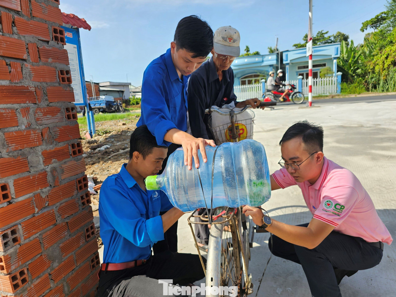 Đoàn viên thanh niên hỗ trợ cụ ông buộc chặt thùng nước trên yên xe đạp để chở về nhà. Ảnh: Hòa Hội