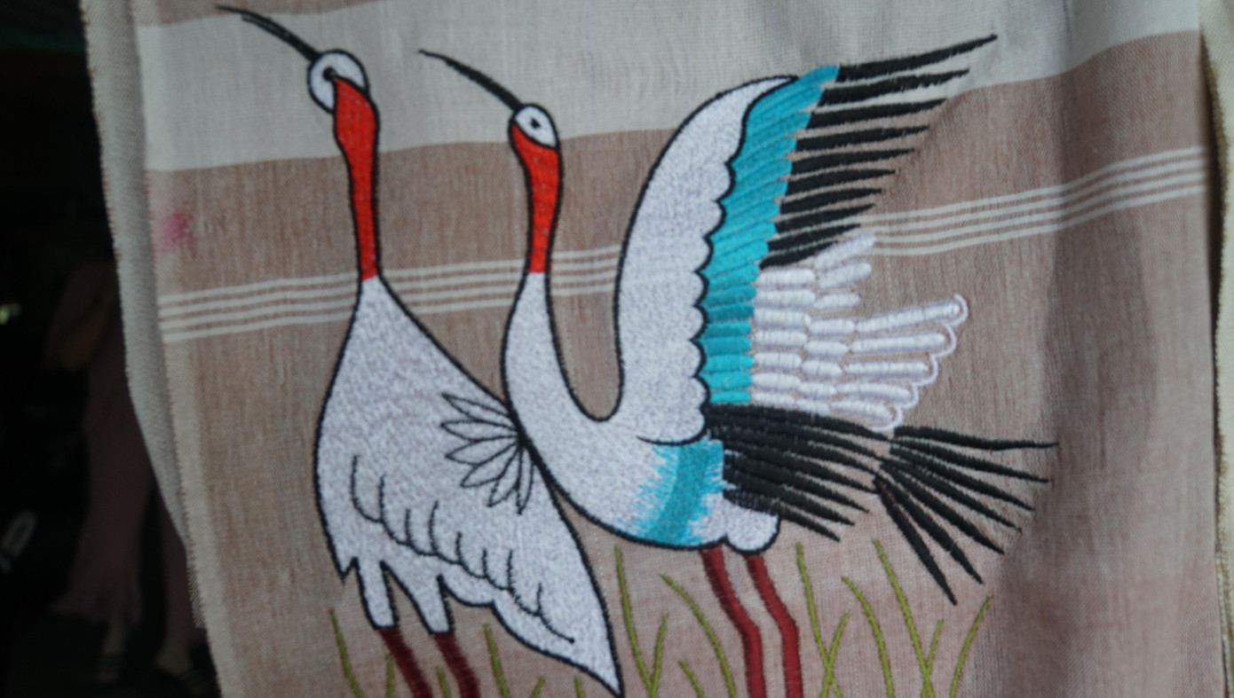 “Khó khăn lớn nhất với người thợ là kích cỡ khăn nhỏ hơn loại truyền thống, lại dệt dày hơn nên máy dệt thường xuyên lỗi, đứt chỉ. Để dệt được chiếc khăn rằn du lịch đầu tiên, tôi mất cả tuần cải tiến, sửa chữa từng chút một", bà nhớ lại. Trong ảnh: Sếu đầu đỏ được thêu trên khăn rằn.