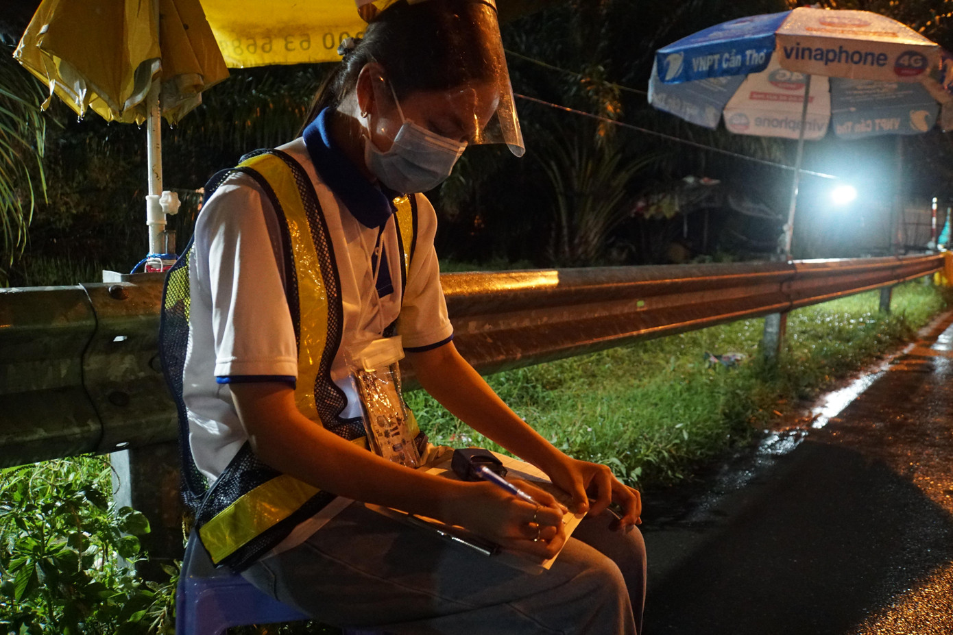 Sau khi phỏng ghi âm phỏng vấn tài xế bằng điện thoại, đợi tạnh mưa tình nguyện viên ghi thông tin vào sổ. - Ảnh: Hòa Hội