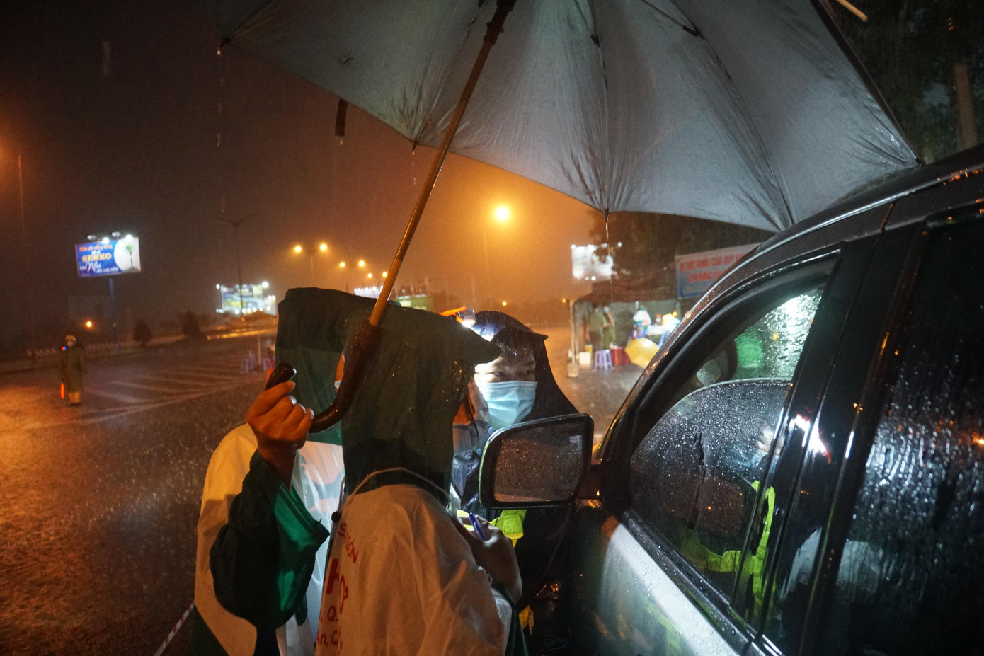 Tình nguyện viên che dù hỗ trợ đồng đội làm nhiệm vụ. - Ảnh: Hòa Hội