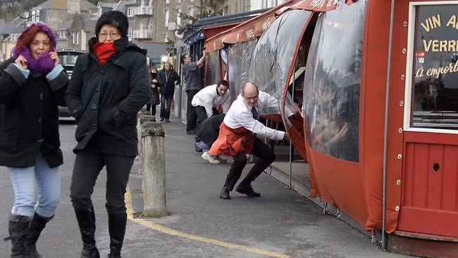 Nhân viên một cửa hàng cafe đóng cửa để bảo vệ khách khỏi gió lớn ở Cancale, Pháp