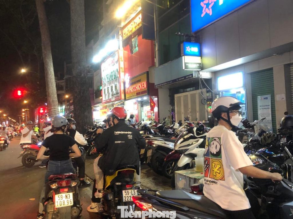 Hàng xe máy xếp kín hết vỉa hè. Một nhóm bạn trẻ chưa tìm được quán ăn vì nơi nào cũng kín chỗ.