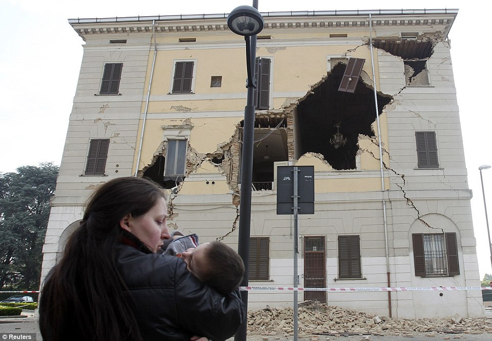 Người phụ nữ bế con đứng nhìn ngôi nhà đã bị trận động đất làm hư hỏng