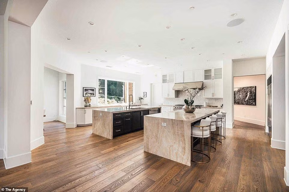 Phòng bếp siêu rộng, với sàn gỗ, ở giữa có chỗ rửa và bàn với bề mặt là đá granit.