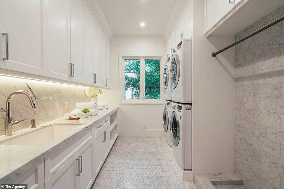 Một phòng giặt lớn có hai máy giặt và hai máy sấy, mặt bàn bằng đá granit, một bồn rửa và tủ màu trắng. Một phòng giặt lớn có hai máy giặt và hai máy sấy, mặt bàn bằng đá granit, một bồn rửa và tủ màu trắng.