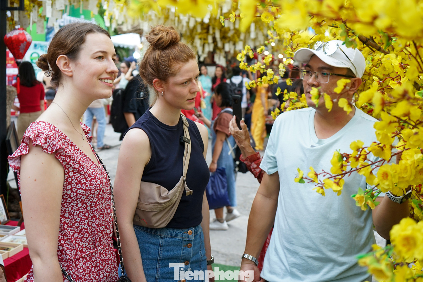 Hai nữ du khách nước ngoài nghe người dân giới thiệu về nguồn gốc của cây mai Hai nữ du khách nước ngoài nghe người dân giới thiệu về nguồn gốc của cây mai