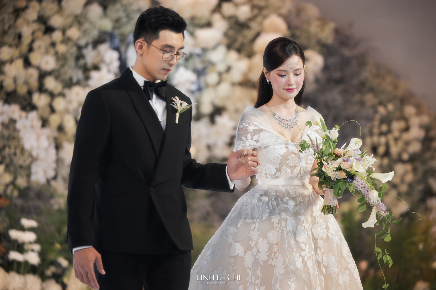 Trước giờ G, Midu và chồng doanh nhân thử trang phục tại bối cảnh ở trung tâm tiệc cưới. Midu mặc váy trễ vai, họa tiết thêu hoa nổi màu trắng.