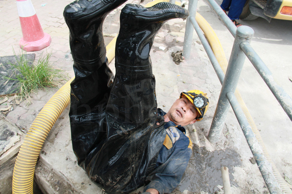 Vừa lên đường, anh Hồ Thanh Sơn ngã lăn ra đường, giơ chân lên trời để nước từ trong người chảy ra ngoài. Bộ quần áo bảo hộ đã rách, không cản được nước bẩn chui vào người. Ảnh: Trường Phong