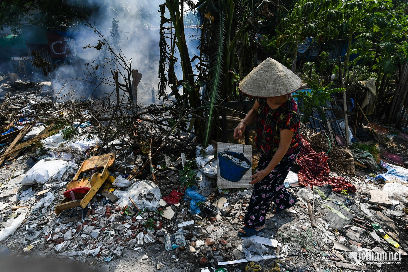 Người phụ nữ trong hình cho biết, bà trồng rau tăng gia ven hồ, ngay cạnh một điểm ngập phế thải. Trưa 31/10, phát hiện đám cháy ở khu lấn chiếm sắp lan đến dãy nhà dân, bà múc từng xô nước để dập lửa. "Không rõ ai là người san lấp trộm nhưng cứ lâu lâu họ lại tập kết đốt phế liệu một lần khiến khói và lửa cháy lan gần vào khu dân cư. Thật sự rất nguy hiểm vì có thể gây cháy lớn", bà bức xúc nói.