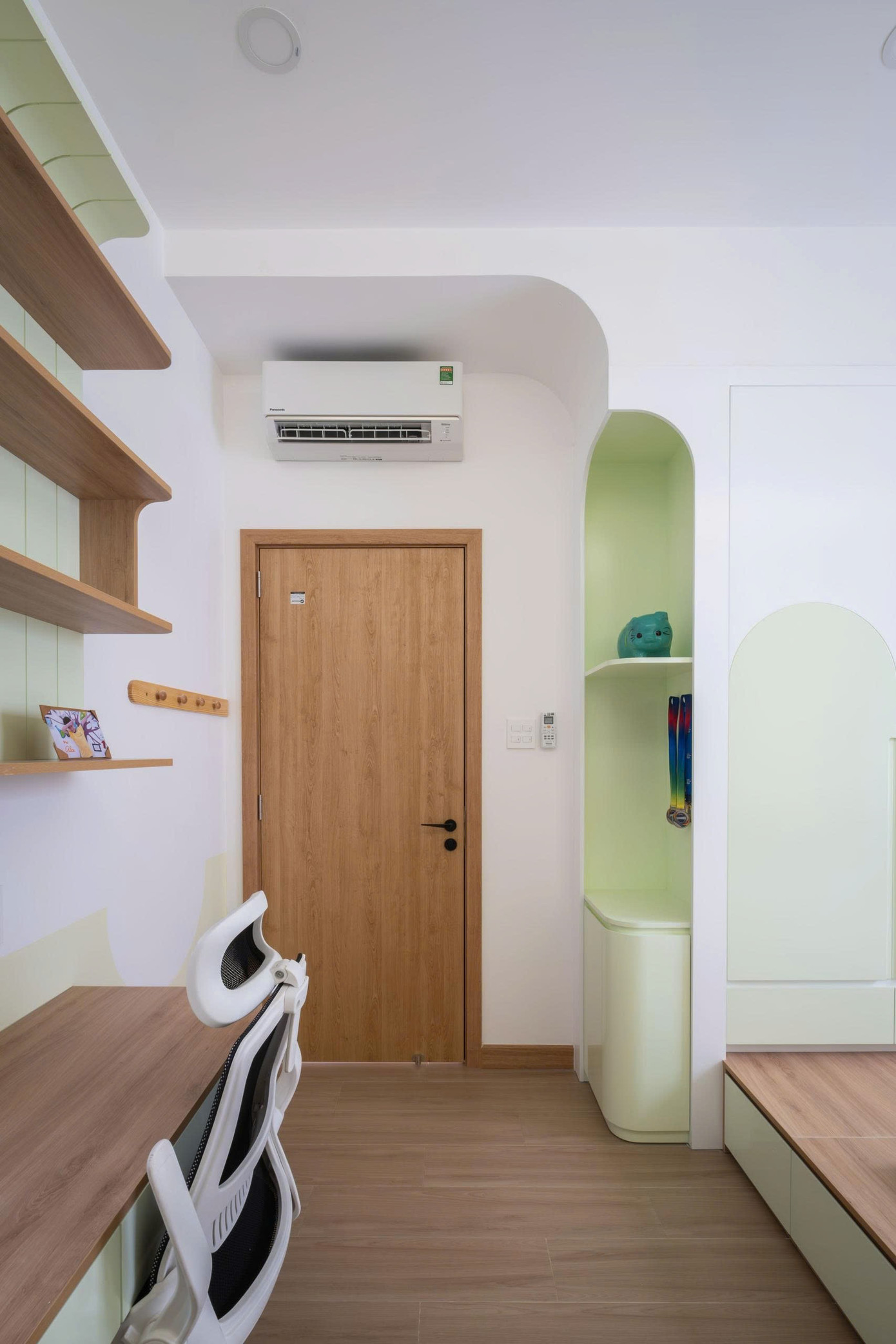 Bàn học và kệ sách được thiết kế nhỏ gọn, phù hợp với vóc dáng của trẻ. Việc sử dụng màu xanh pastel cho khu vực này giúp phân định không gian chức năng và kích thích sự sáng tạo.