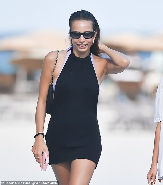 Sau đó, người đẹp 9x mặc chiếc váy đen cổ yếm ra ngoài và đi dạo bãi biển.