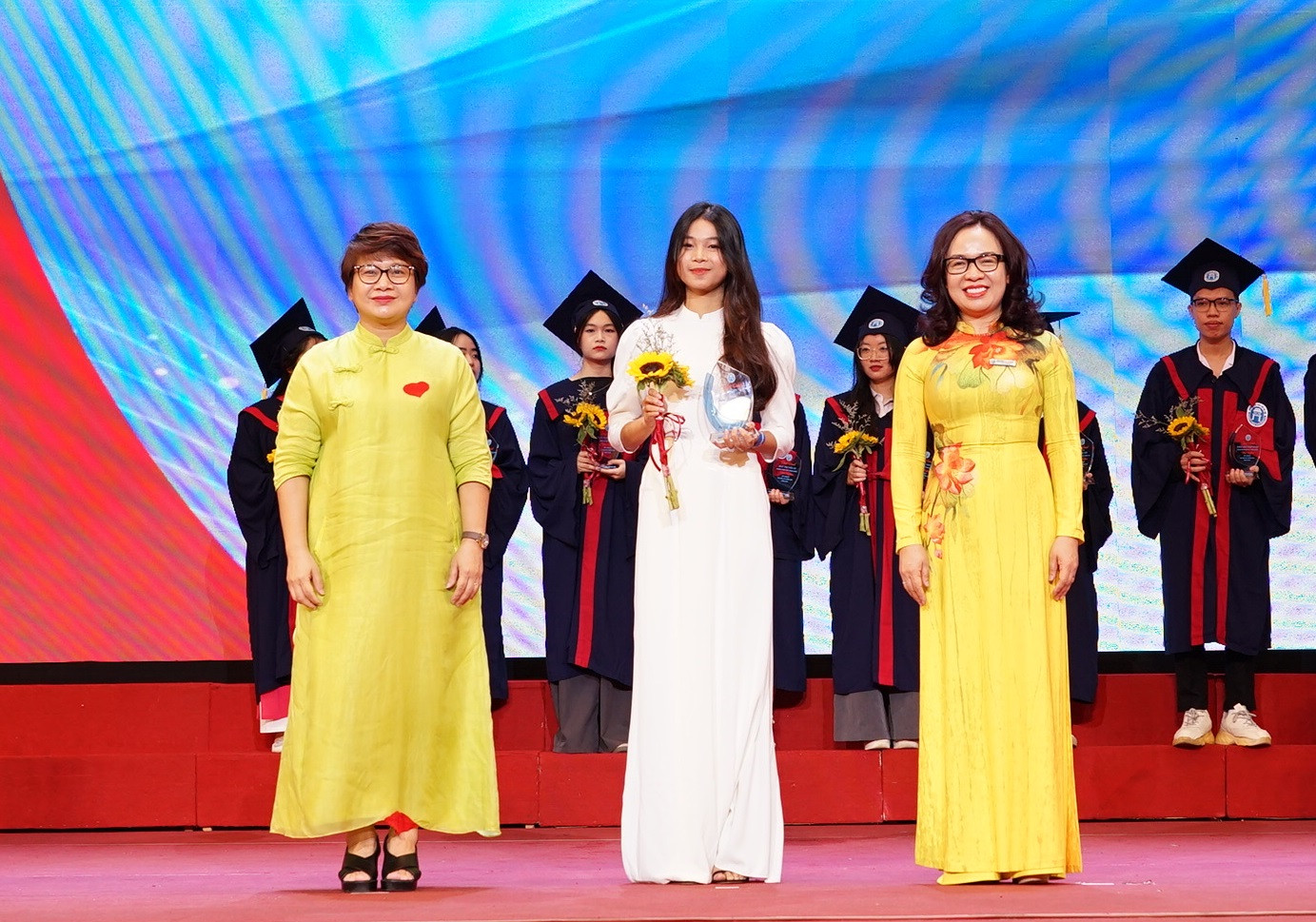 PGS.TS Nguyễn Thu Thủy, Vụ trưởng Vụ giáo dục ĐH (ngoài cùng bên trái) và PGS.TS Nguyễn Thị Nhung, Hiệu trưởng Trường ĐH Mở Hà Nội trao biểu trưng và tặng hoa cho sinh viên thủ khoa kỳ tuyển sinh năm 2024 tại lễ khai giảng.