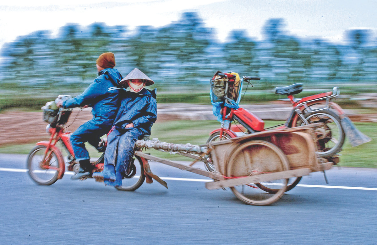 Một cặp vợ chồng ở ngoại thành Hà Nội đang trên đường về nhà sau khi chở hàng vào nội thành. Để tiết kiệm xăng, người chồng chở cả vợ và xe của vợ ở phía sau Một cặp vợ chồng ở ngoại thành Hà Nội đang trên đường về nhà sau khi chở hàng vào nội thành. Để tiết kiệm xăng, người chồng chở cả vợ và xe của vợ ở phía sau