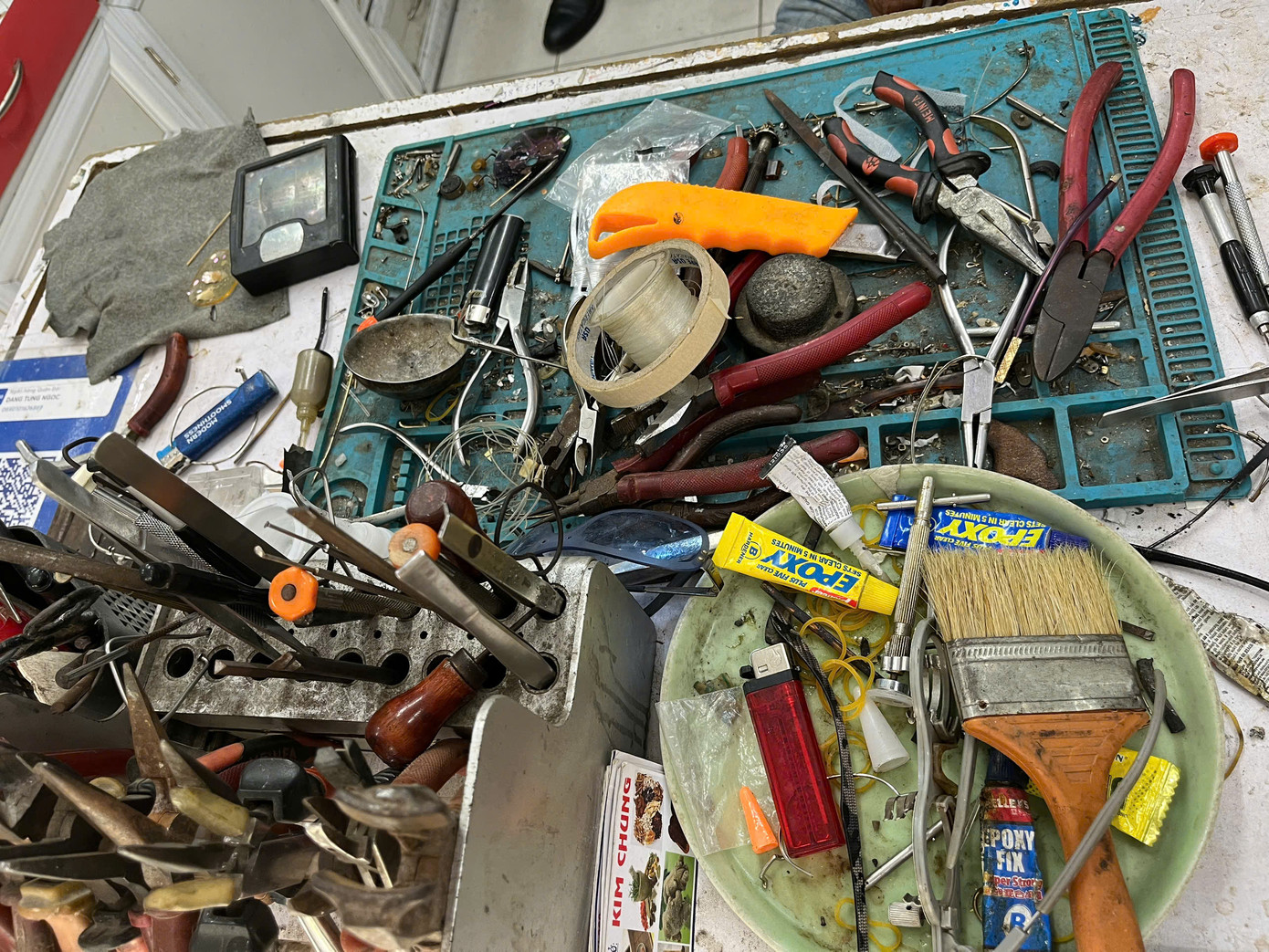 Rất nhiều dụng cụ làm việc được ông để trên chiếc bàn cũ.