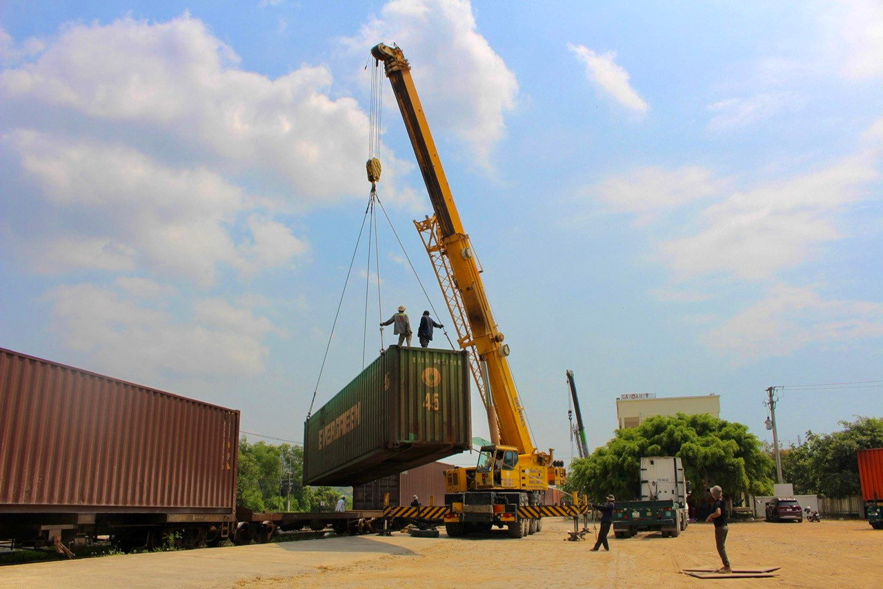 Dưới cái nắng gay gắt, các công nhân cùng cần cẩu liên tục bốc những container hàng từ tàu hỏa lên xe đầu kéo để trung chuyển.
