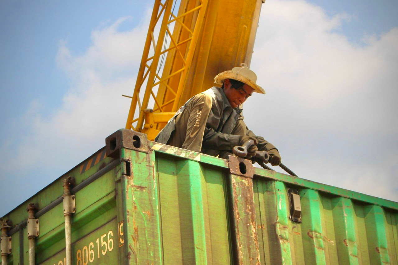 Trước khi những thùng hàng được kéo lên, các công nhân phải buộc dây cáp cẩu hàng thật cẩn thận để tránh xảy ra sai sót. Hàng hóa sẽ được cẩu 100 tấn dỡ xuống xe đầu kéo.