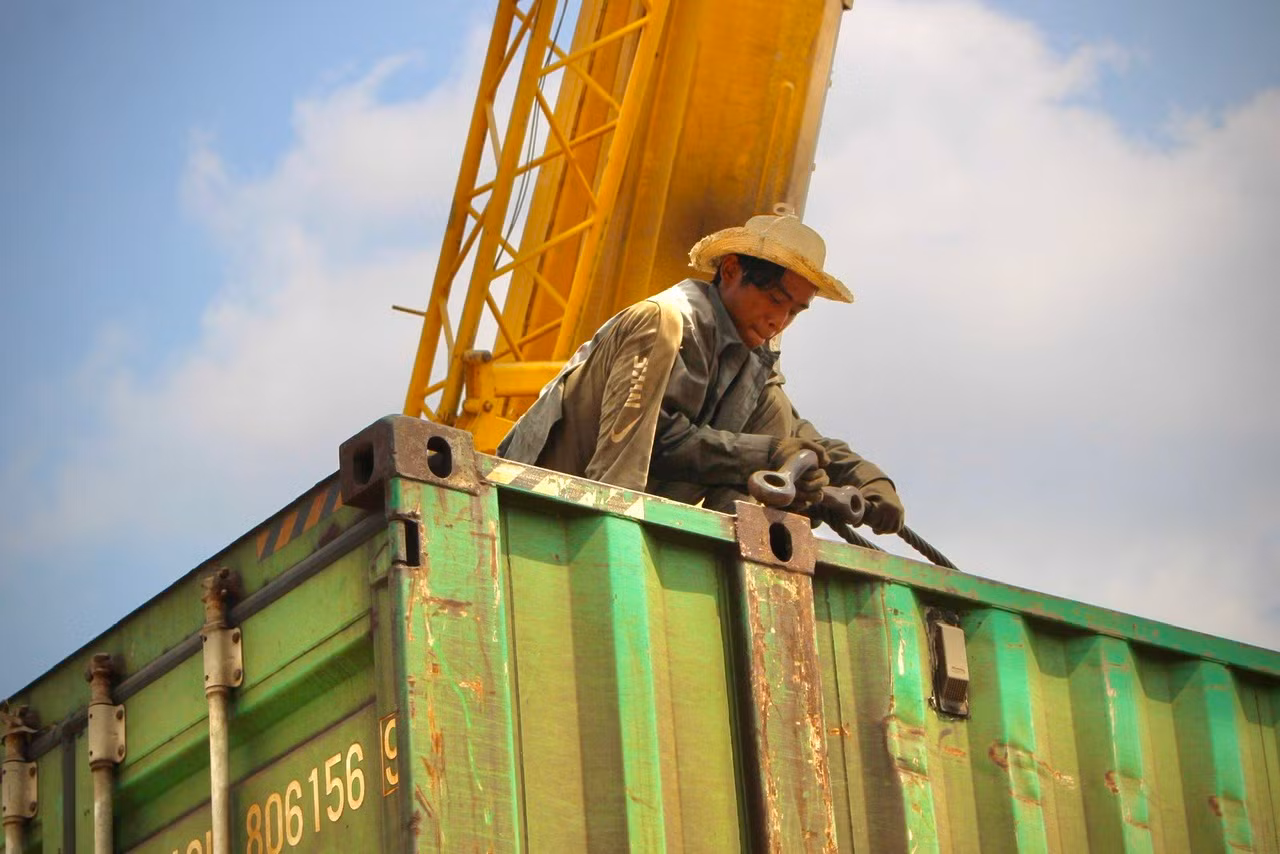 Trước khi những thùng hàng được kéo lên, các công nhân phải buộc dây cáp cẩu hàng thật cẩn thận để tránh xảy ra sai sót. Hàng hóa sẽ được cẩu 100 tấn dỡ xuống xe đầu kéo.