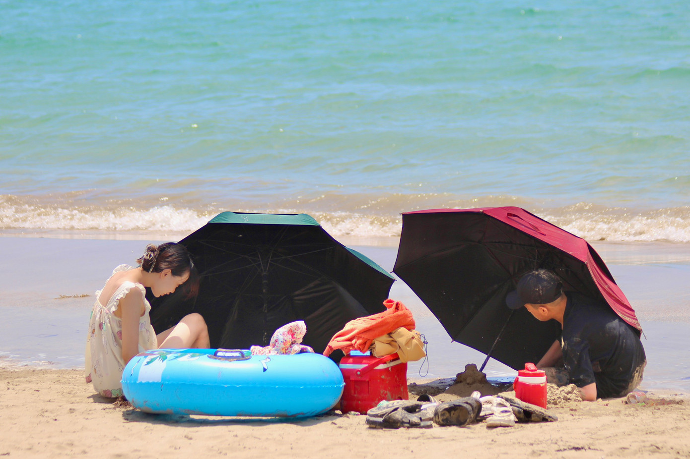 2 bạn trẻ che dù "núp" nắng, vui đùa trên cát.
