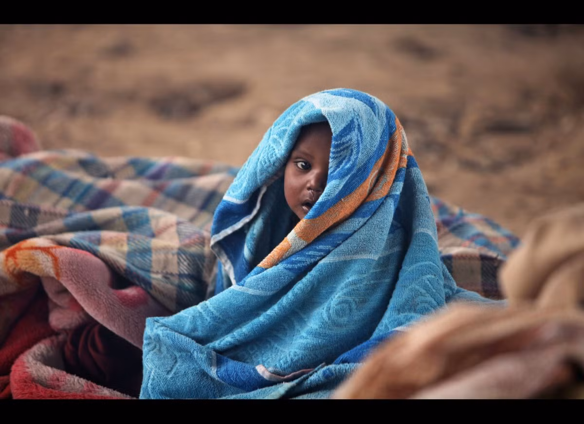 Em bé vô gia cư bọc mình trong chăn ở căn lều tạm dưới chân cầu vượt ở Jammu, Ấn Độ