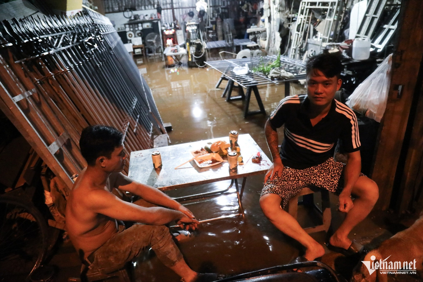 Cơ sở kinh doanh nhôm của anh Phúc (áo đen) bị ngập hoàn toàn. Sau khi các vật dụng đã được kê cao, hai người đàn ông này mới ngồi ăn tối. Cơ sở kinh doanh nhôm của anh Phúc (áo đen) bị ngập hoàn toàn. Sau khi các vật dụng đã được kê cao, hai người đàn ông này mới ngồi ăn tối.