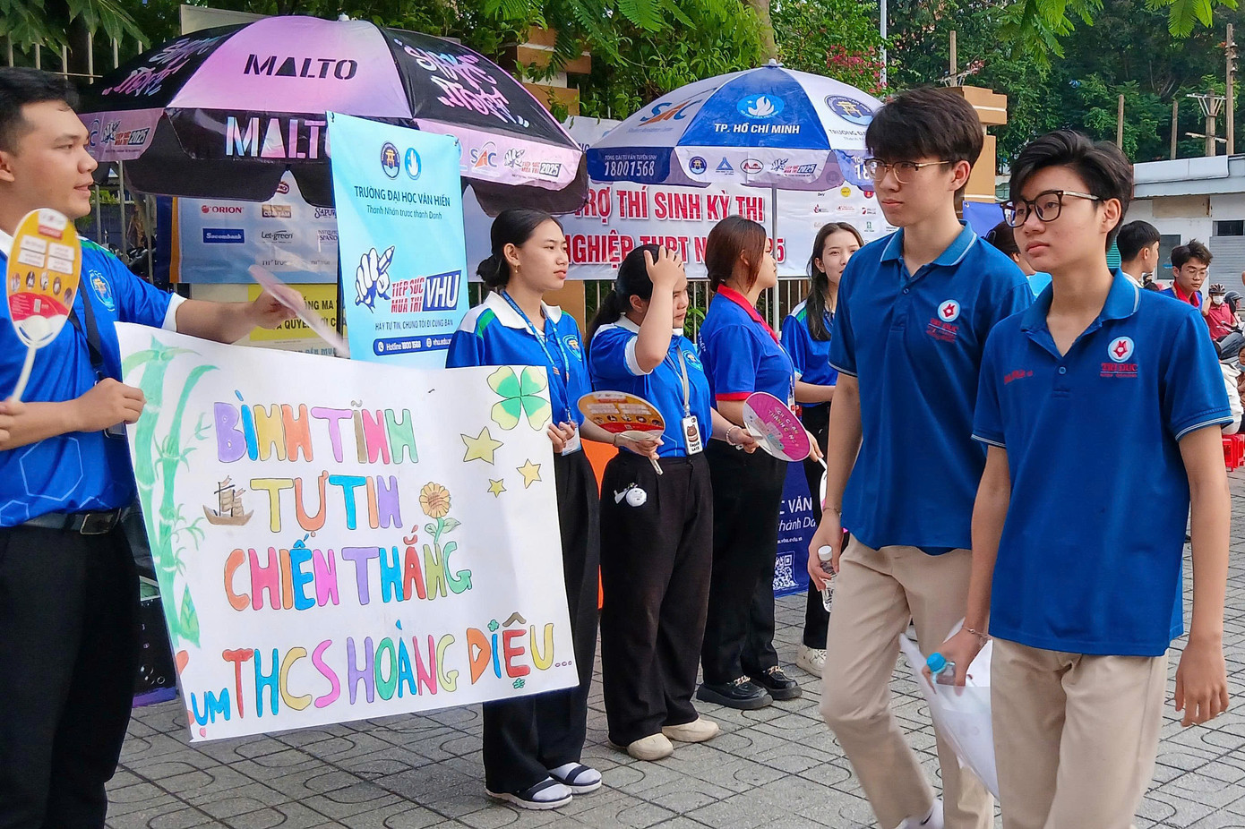 Tại cổng điểm thi, các bạn sinh viên tình nguyện chương trình 'Tiếp sức mùa thi' có mặt từ sớm, hỗ trợ hướng dẫn đường đi. Sinh viên tình nguyện còn trông giữ tài sản, phát nước, động viên tinh thần, điều phối giao thông.