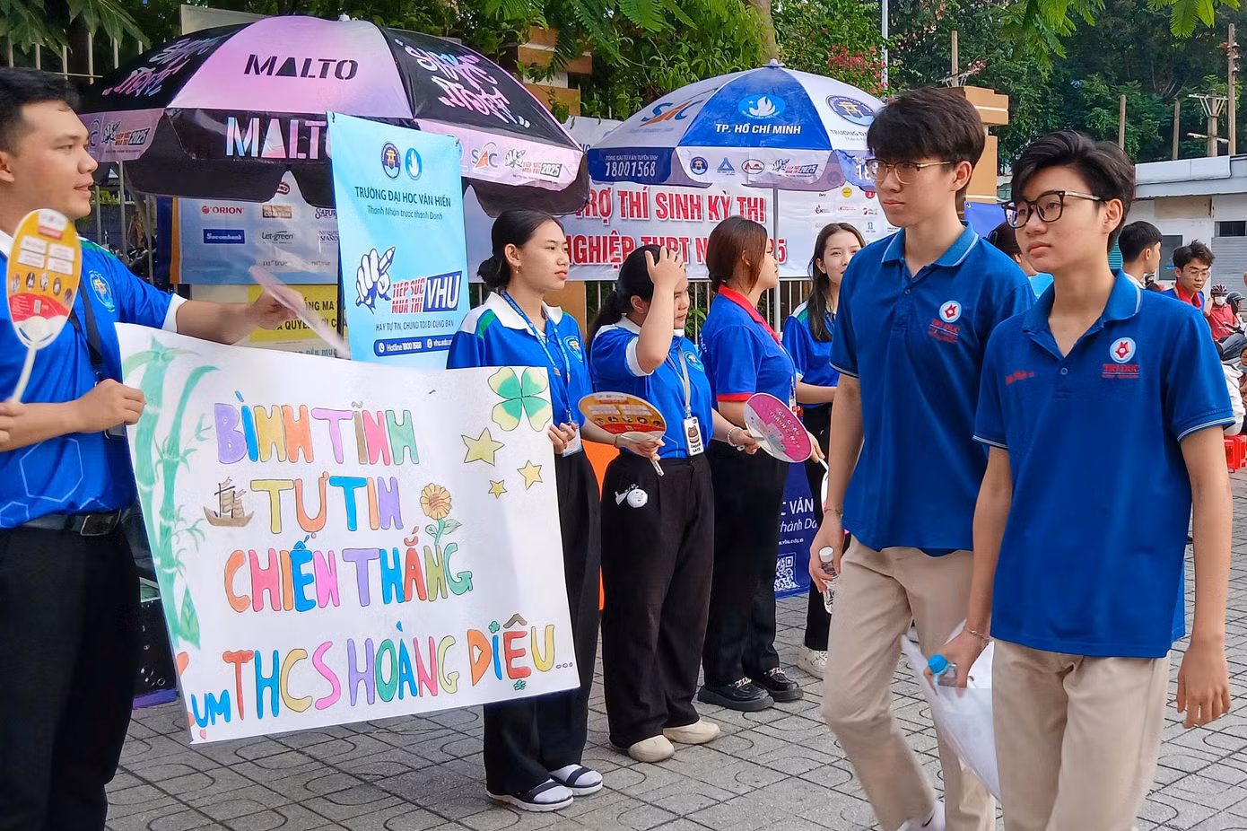 Tại cổng điểm thi, các bạn sinh viên tình nguyện chương trình 'Tiếp sức mùa thi' có mặt từ sớm, hỗ trợ hướng dẫn đường đi. Sinh viên tình nguyện còn trông giữ tài sản, phát nước, động viên tinh thần, điều phối giao thông.