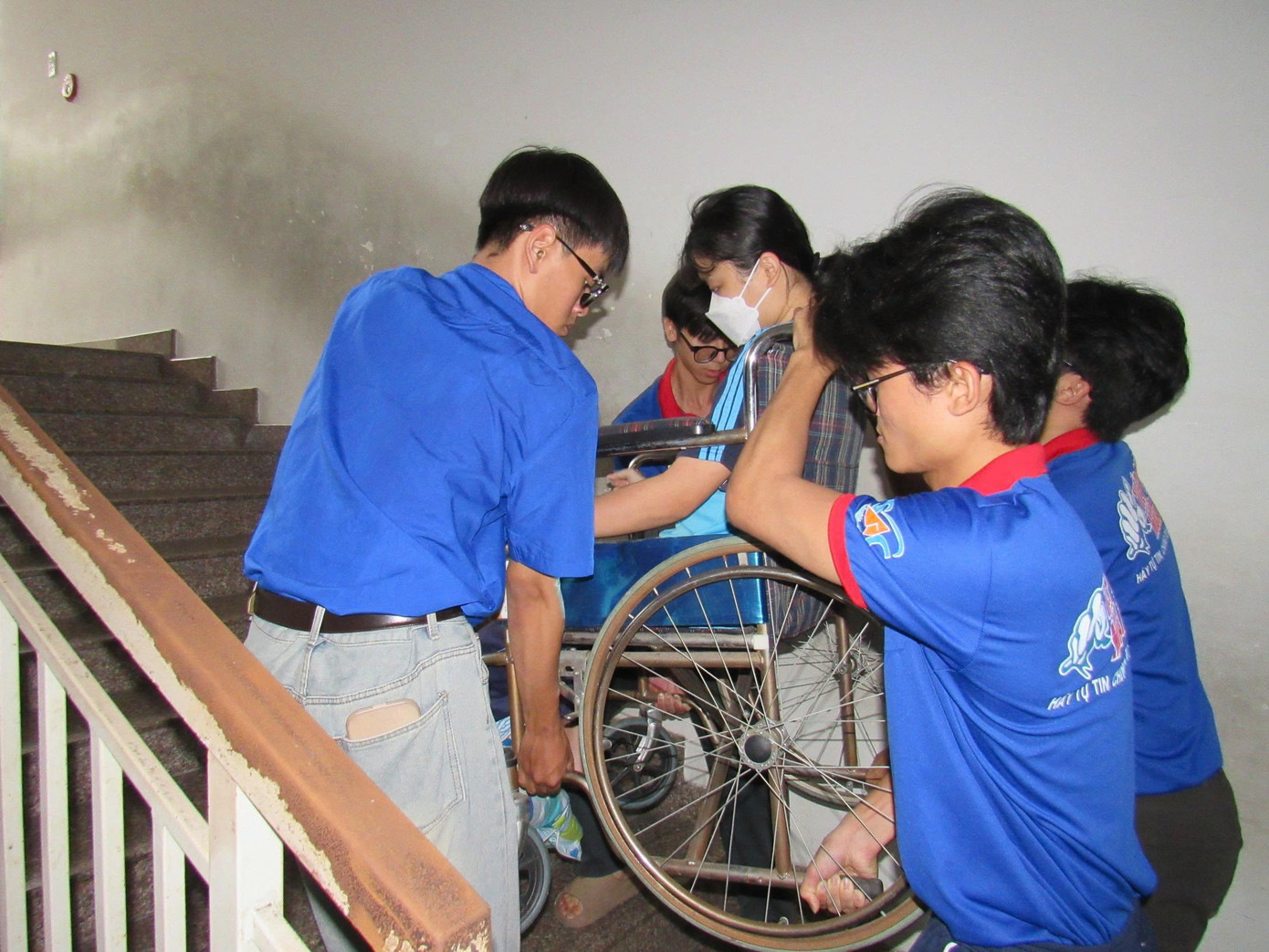 Nhóm tình nguyện viên phối hợp khiêng xe lăn đưa thí sinh lên phòng thi tại điểm trường THCS Trần Huy Liệu (Q. Phú Nhuận). (Ảnh: Đăng Khoa)