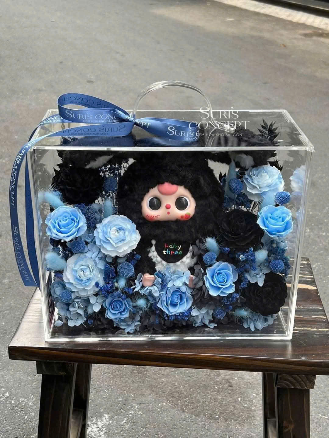 Mẫu quà tặng độc đáo với tông màu xanh – đen cá tính, kết hợp giữa hoa vĩnh cửu sang trọng và búp bê Baby Three dễ thương, được đặt trong hộp mica cao cấp.