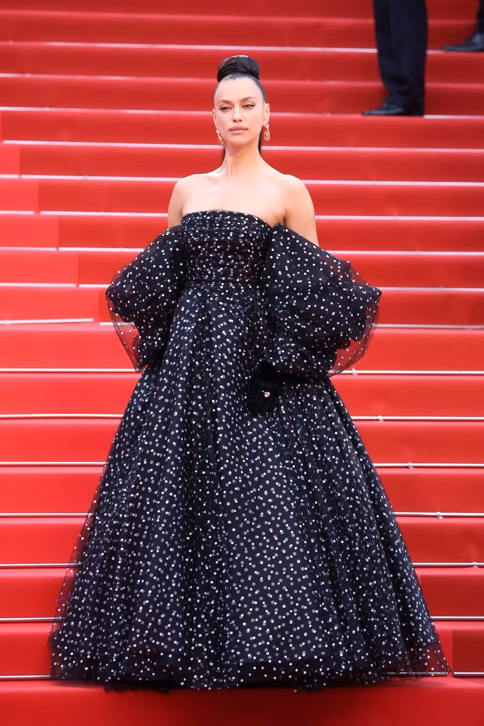 Irina Shayk ngọt ngào và nữ tính trong chiếc váy quây đen chấm bi trắng bồng bềnh. Phong cách này khác hẳn với hình ảnh nóng bỏng thường thấy của bạn gái cũ Ronaldo. Điểm trừ là kiểu tóc của siêu mẫu Nga khá khó hiểu và không ăn khớp với bộ cánh. Ảnh: Getty Images.