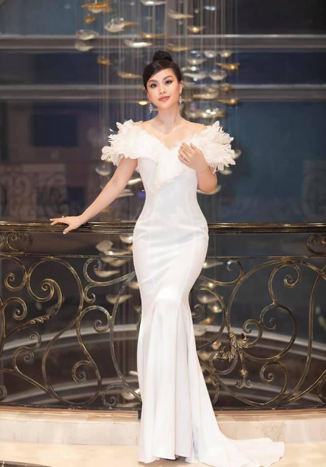 Á hậu Diễm Trang diện váy đuôi cá màu trắng đính lông vũ cầu kỳ khi đảm nhận vai trò MC trong một chương trình.