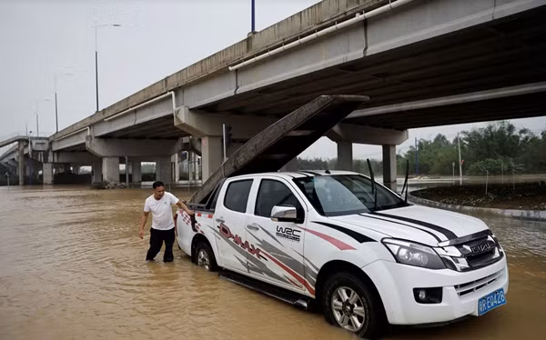 Ảnh Huang Jingrong buộc một chiếc thuyền vào xe ô tô khi thấy mưa lớn. Ảnh: Tingshu Wang/ Reuters.